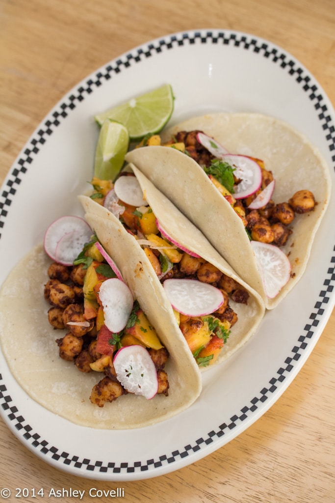 Overhead view of a plate with 3 Spiced Chickpea Tacos with Cilantro-Peach Relish and lime wedges.