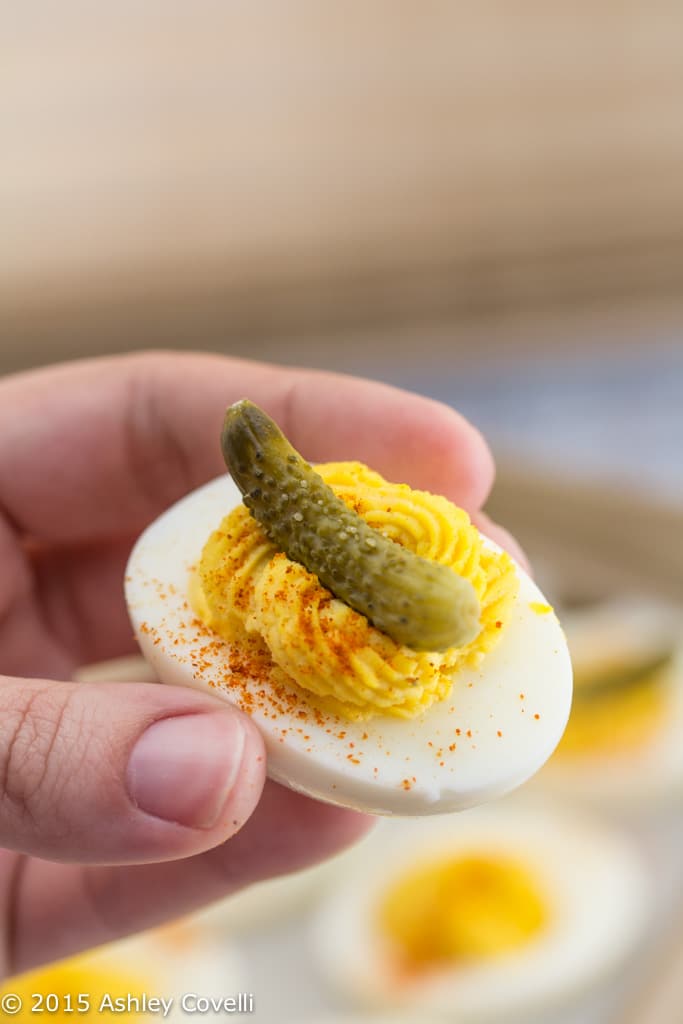 Close-up of someone holding a deviled egg with a cornichon on top.