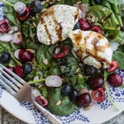 Overhead view of a plate of salad topped with fruit, vegetables, and burrata cheese drizzled with aged balsamic.