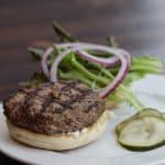 Lamb Burger on a plate with pickles and toppings.