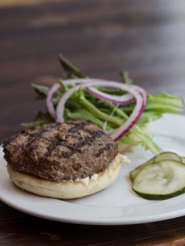 Lamb Burger on a plate with pickles and toppings.