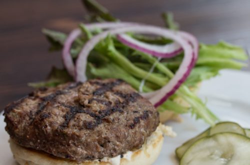 Lamb Burger on a plate with pickles and toppings.
