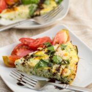 3/4 view of a slice of zoodle frittata topped with fresh herbs and a balsamic tomato salad.