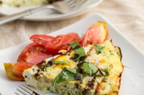 3/4 view of a slice of zoodle frittata topped with fresh herbs and a balsamic tomato salad.