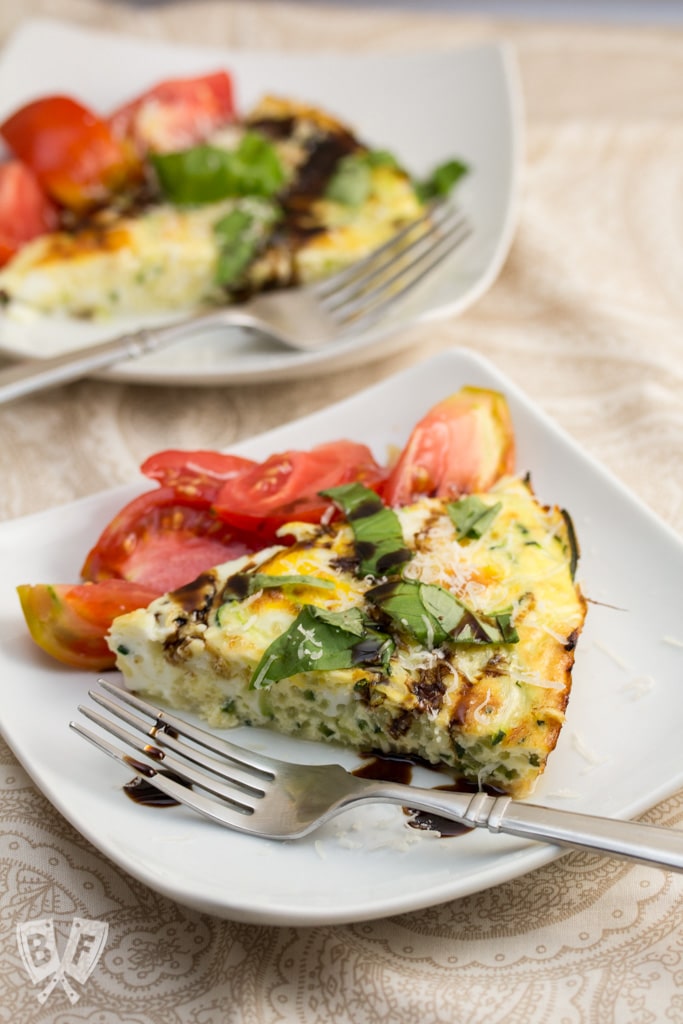 ¾ view of a slice of zoodle frittata topped with fresh herbs and a balsamic tomato salad.