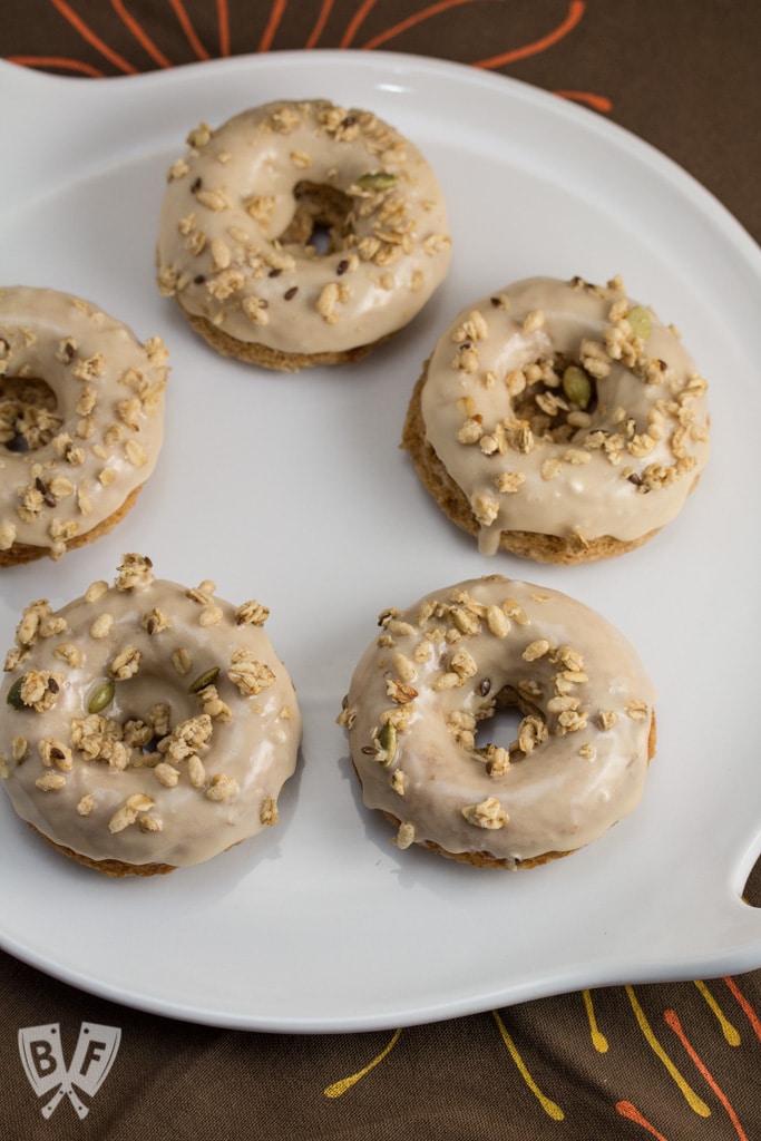 Baked Apple Spice Donuts with Maple Frosting and Pumpkin Granola (#ad): Crunchy granola is a perfect topping for these apple + Greek yogurt infused baked donuts. A great breakfast or dessert recipe to use your fall apple bounty! #StonyfieldBlogger