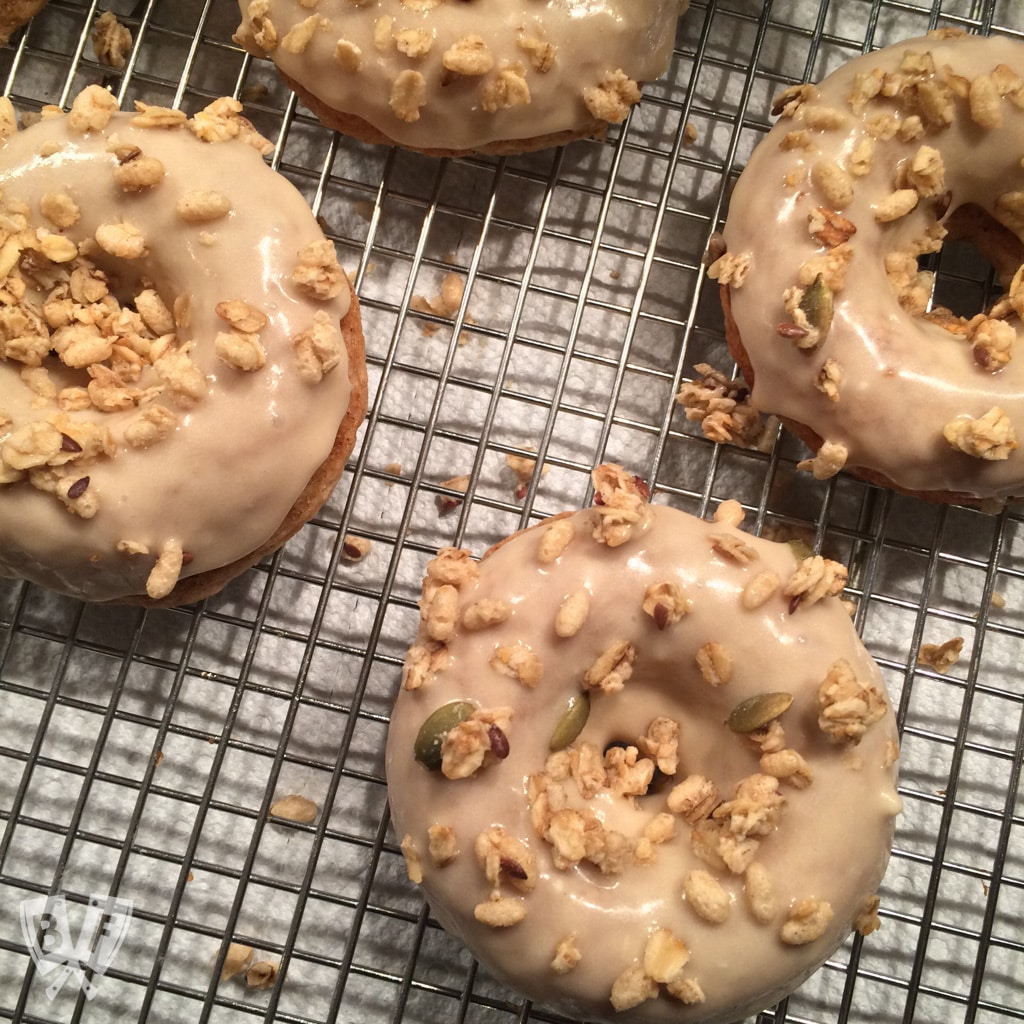 Baked Apple Spice Donuts with Maple Frosting and Pumpkin Granola (#ad): Crunchy granola is a perfect topping for these apple + Greek yogurt infused baked donuts. A great breakfast or dessert recipe to use your fall apple bounty! #StonyfieldBlogger