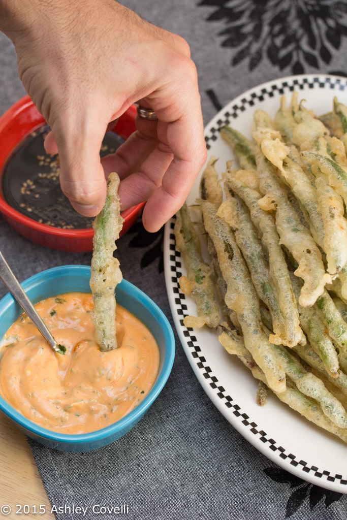 Dipping a tempura green bean into a dipping sauce.