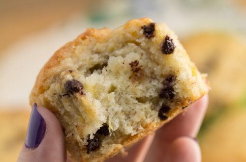 Hand holding a banana chocolate chip muffin with a bite taken out of it.