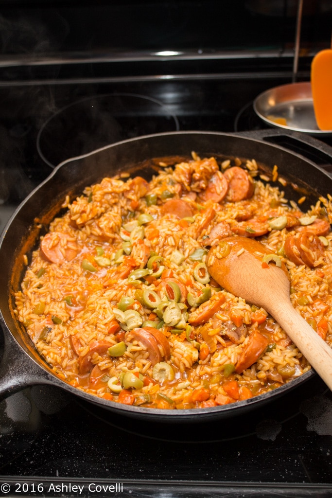 Stirring a Spanish chicken + sausage dish in a cast iron skillet.