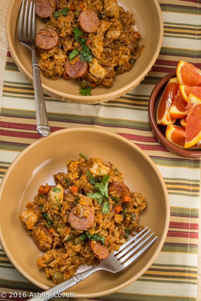 2 bowls with Spanish chicken + sausage with a bowl of oranges.