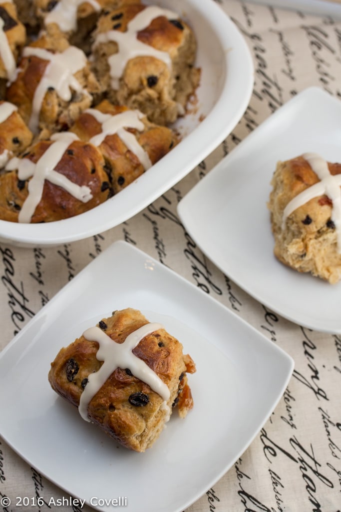 Tray of hot cross buns with 2 served on plates.