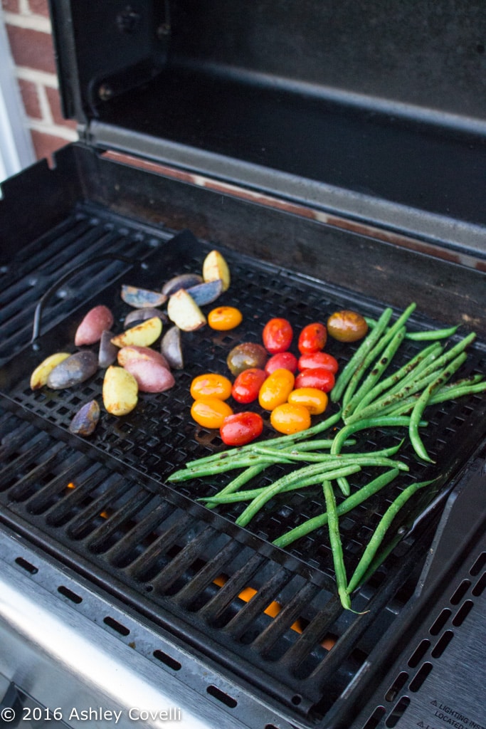 A grill with colorful potatoes, tomatoes, and green beans.