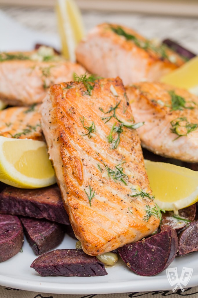 Platter of seared salmon with dill and lemon over purple sweet potatoes.