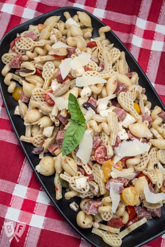 Platter of pasta salad with salami, Parmesan cheese, tomatoes, and basil.