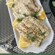 Overhead view of a platter of grilled sand shark garnished with lemon wedges and fresh dill.