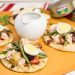 3 mini naan breads topped with grilled Niçoise salad ingredients along with a pitcher of vinaigrette and tuna cans in the background.