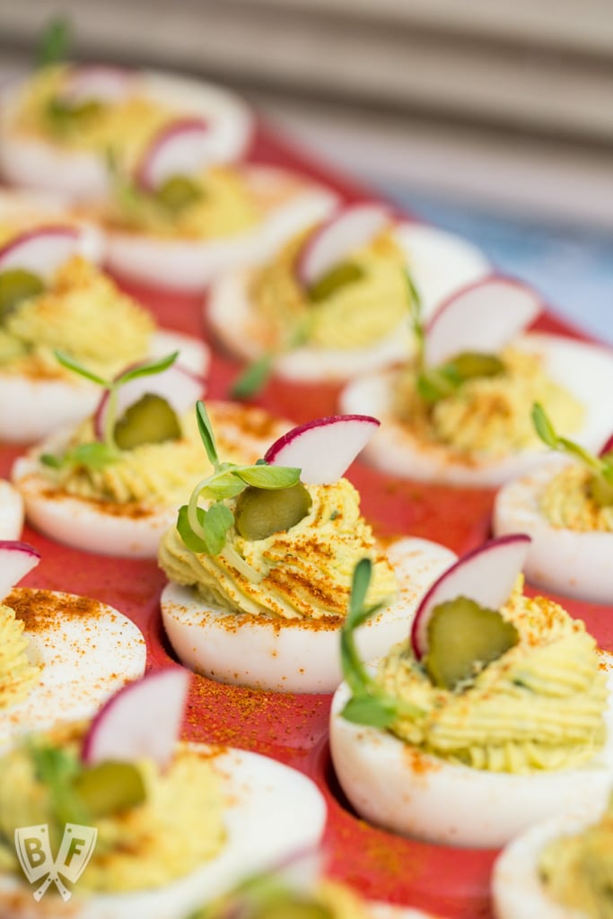 Platter of deviled eggs with colorful garnishes.