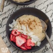 Overhead view of a bowl of porridge decorated with dried strawberries and coconut flakes.