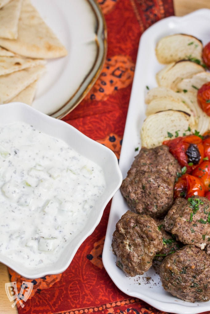 Overhead view of a Persian meal with yogurt, kebab, veggies, and pita.