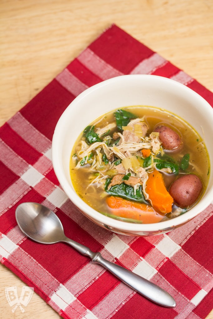 Bowl of Instant Pot chicken, bacon, and potato soup with a spoon alongside.