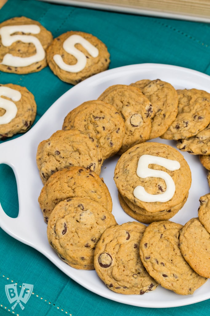 Platter of chocolate chip cookies with the number 5 written in icing on a few of them.