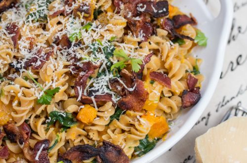 Bowl of red lentil fusilli with bacon, butternut squash, and spinach topped with Parmesan cheese.