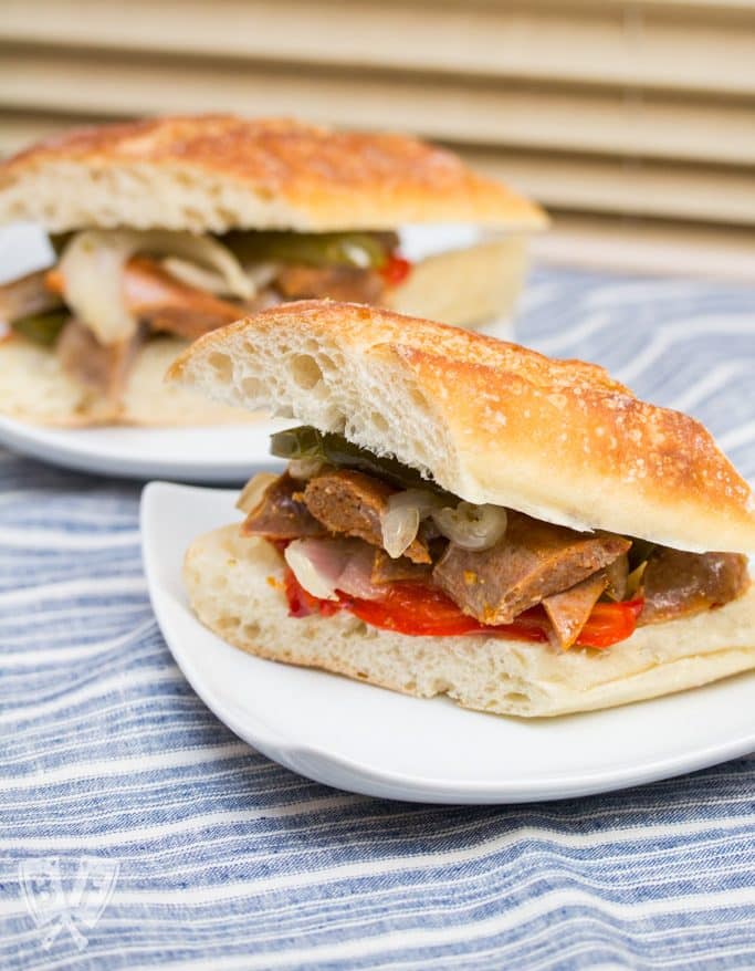 Sausage and peppers served as sandwiches on 2 plates.