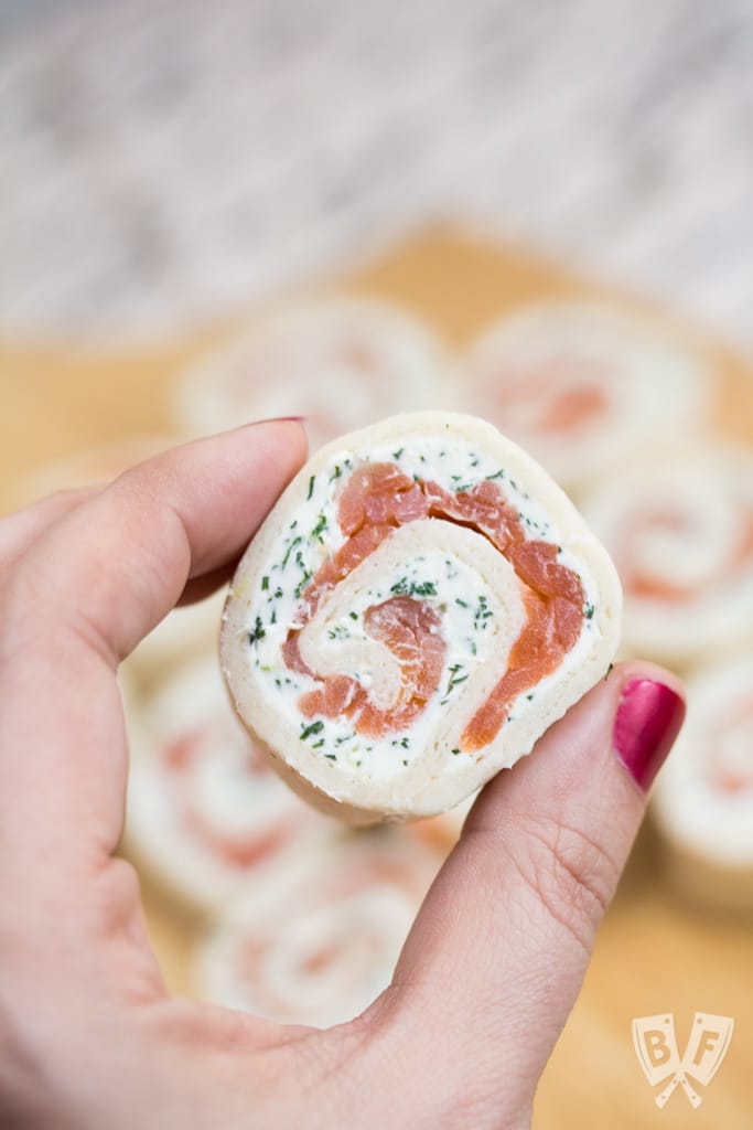 Close-up of a hand holding a smoked salmon roll-up.