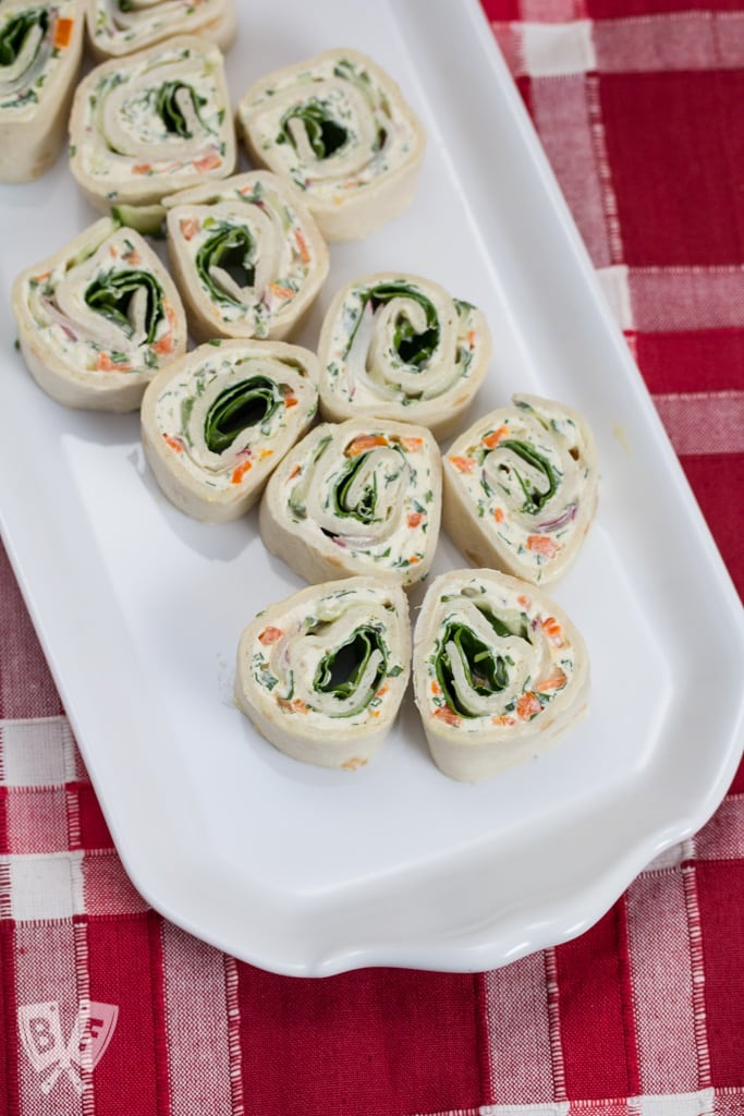 Overhead view of a platter of tortilla roll-ups with cream cheese and vegetables.