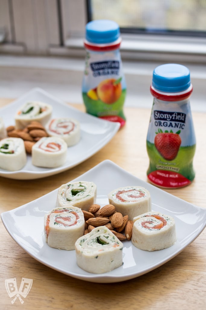 Plates of tortilla roll-ups and nuts served with smoothie bottles.