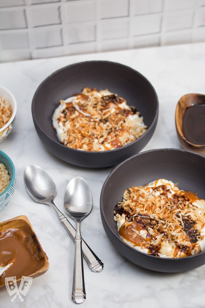 2 bowls of yogurt topped with chocolate, coconut, caramel, and Rice Krispies cereal.