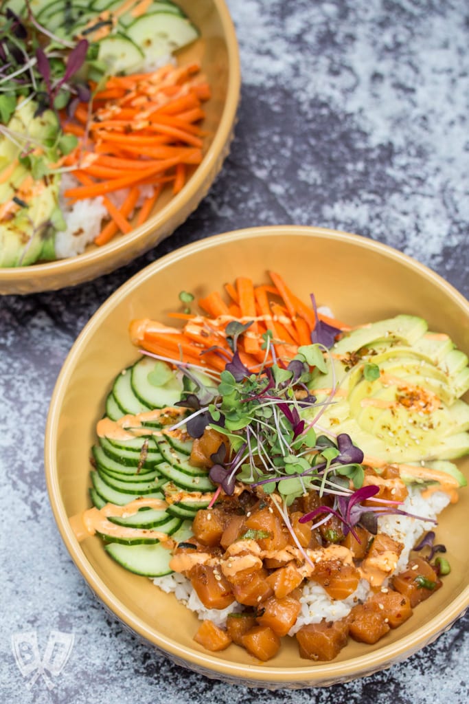 Two spicy salmon poke bowls with rice and colorful toppings.