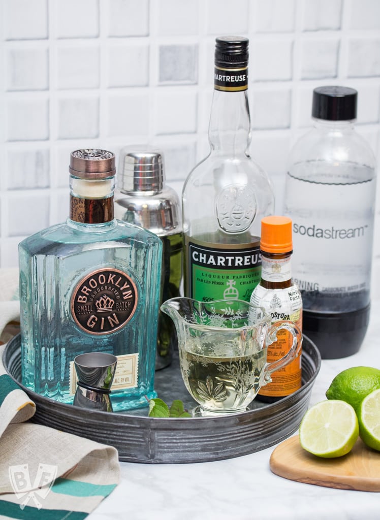 A tray with bottles of ingredients for a gin cocktail with garnishes off to the side.