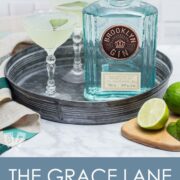 2 gin cocktails on a tray with a bottle of gin and garnishes.