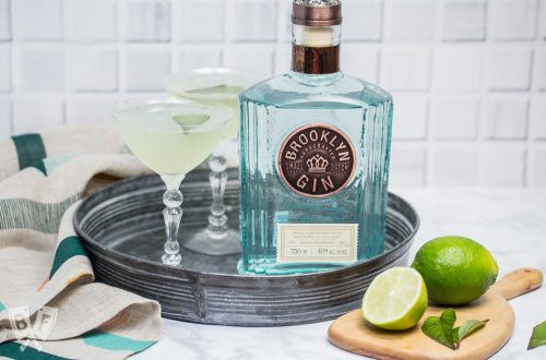 2 gin cocktails on a tray with a bottle of gin and garnishes.