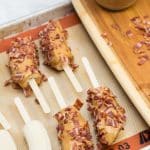 Banana halves on popsicle sticks coated in peanut butter and bacon.