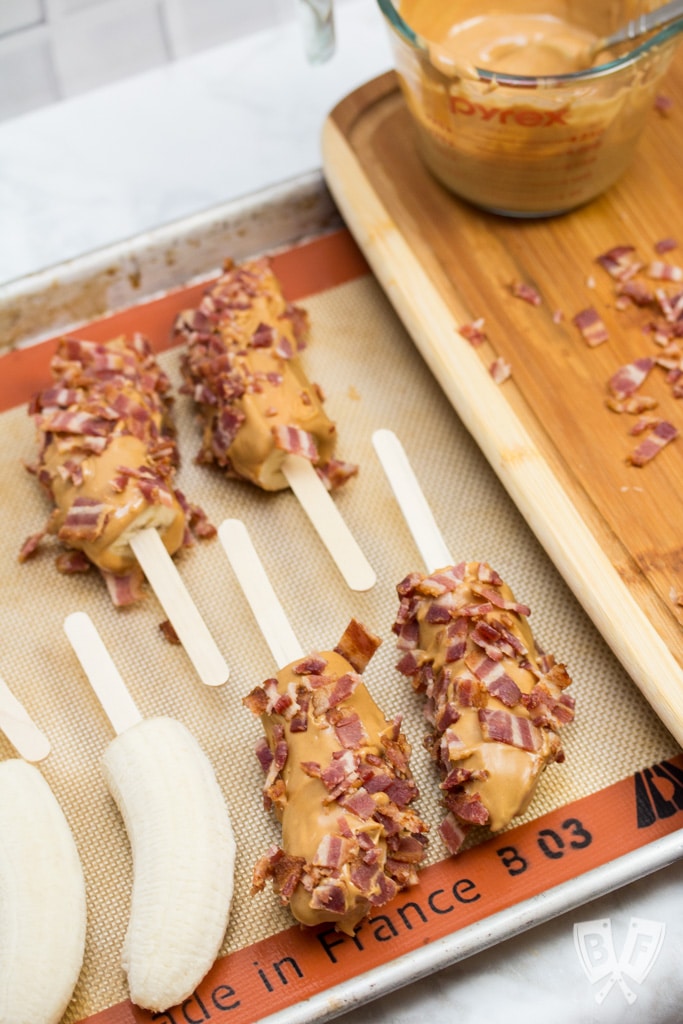 Banana halves on popsicle sticks coated in peanut butter and bacon.