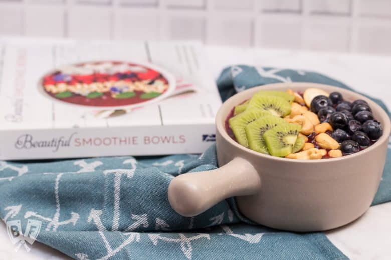 Smoothie bowl topped with fresh fruit and cashews in front of a book about smoothie bowls.