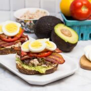 Side view of a platter with 2 open-faced TABLET Sandwiches (Tuna Avocado Bacon Lettuce Egg Tomato) and ingredients off to the sides.