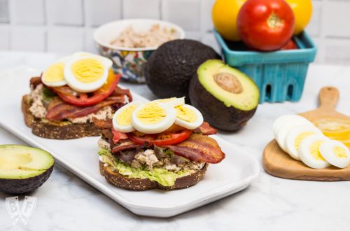 Side view of a platter with 2 open-faced TABLET Sandwiches (Tuna Avocado Bacon Lettuce Egg Tomato) and ingredients off to the sides.