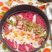 Overhead view of brightly colored smoothie bowls with tropical garnishes sprinkled on top.