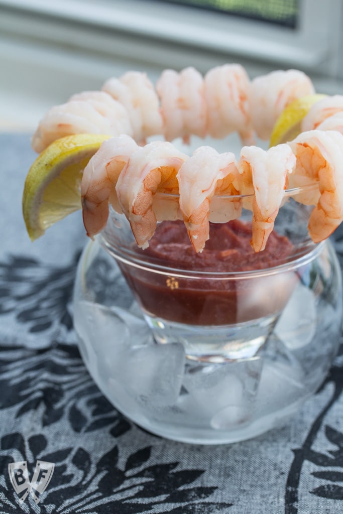 Shrimp cocktail arranged around the rim of a glass with lemon wedges.