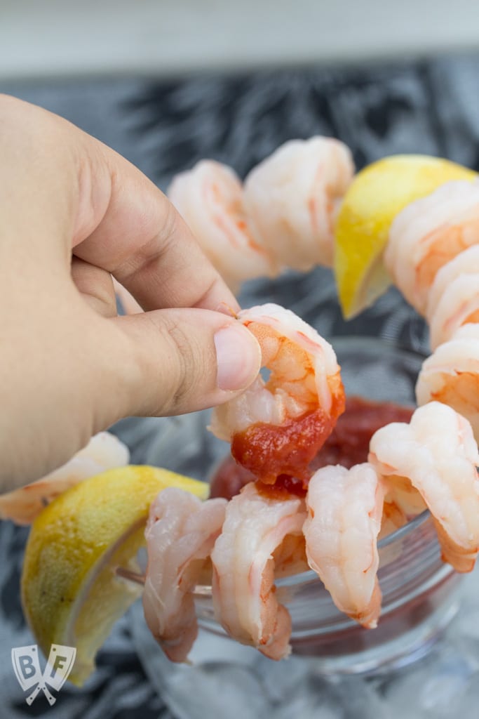 Hand dipping shrimp into cocktail sauce.