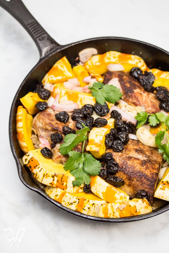 Overhead view of a cast iron skillet with spiced pork tenderloin, squash, and dried cherries.