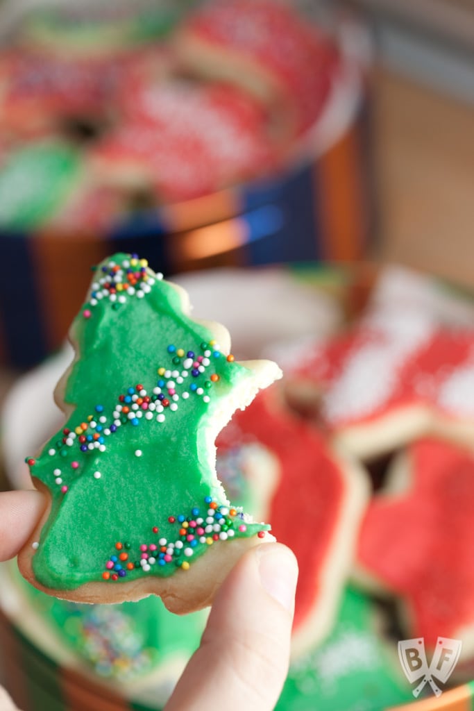 Holding a decorated, Christmas tree-shaped cookie with a bite taken out of it.