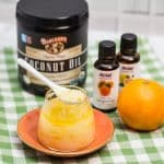 A spoon in a glass jar full of homemade salt scrub surrounded by the products used to make it.