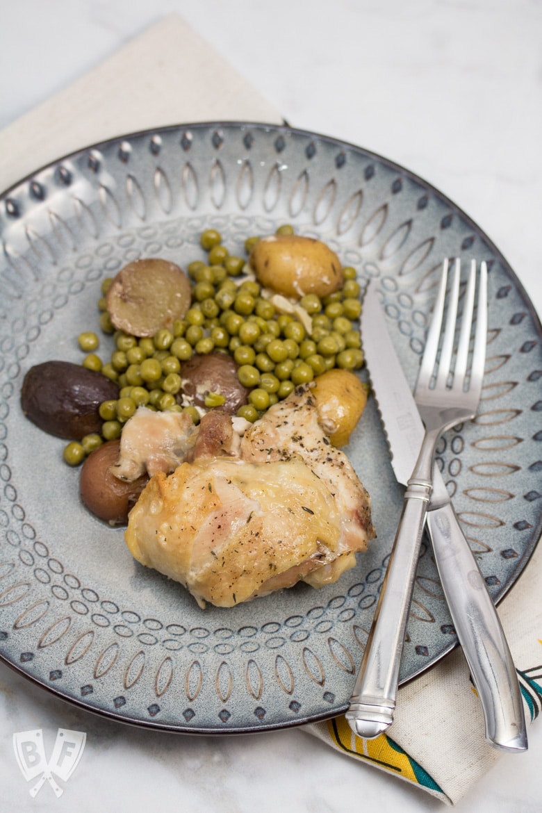 Dinner plate with chicken thigh, peas, and potatoes with a fork and knife off to the side.