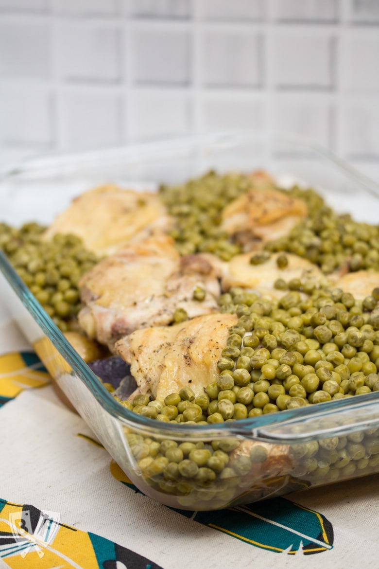 ¾ view of a casserole dish filled with baked chicken thighs, peas, and potatoes.