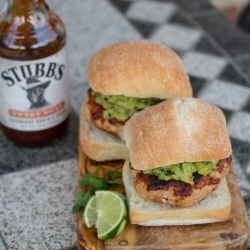 Turkey burgers with guacamole and barbecue sauce with lime wedges alongside.